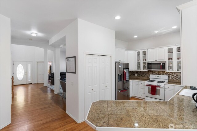 kitchen with glass insert cabinets, light wood-style floors, tile countertops, appliances with stainless steel finishes, and tasteful backsplash