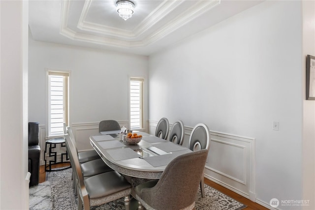 dining room with ornamental molding, wainscoting, a decorative wall, wood finished floors, and a raised ceiling