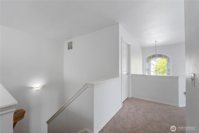 hall featuring baseboards, an upstairs landing, visible vents, and carpet floors