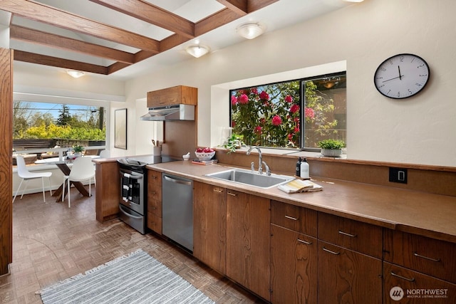 kitchen with appliances with stainless steel finishes, a sink, light countertops, under cabinet range hood, and beamed ceiling