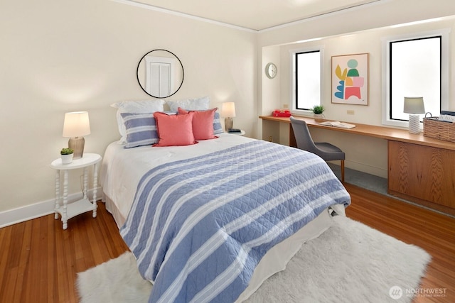 bedroom featuring built in study area, baseboards, crown molding, and wood finished floors