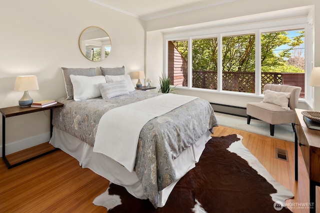 bedroom with visible vents, crown molding, wood finished floors, baseboards, and a baseboard radiator