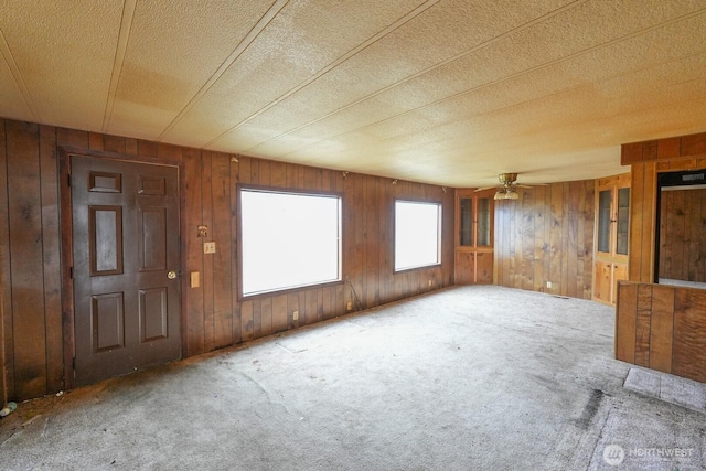 empty room with wooden walls, a ceiling fan, and carpet