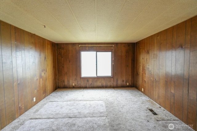carpeted empty room with wood walls and visible vents