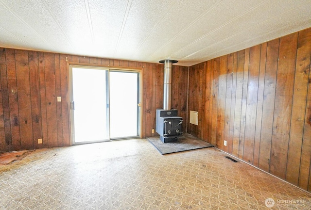 unfurnished living room with visible vents, wood walls, and a wood stove