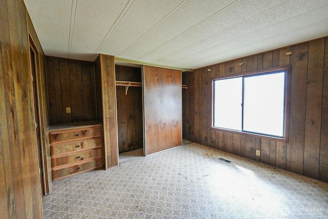 unfurnished bedroom with wooden walls, visible vents, and a closet