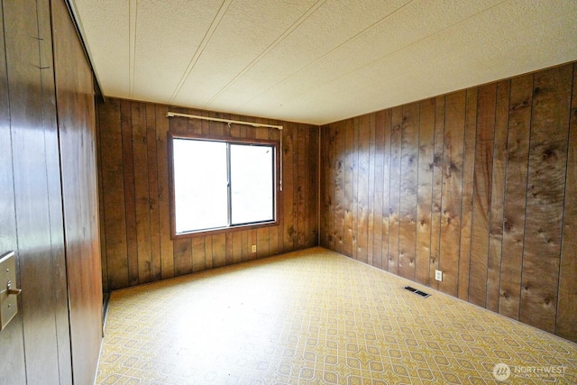 unfurnished room featuring visible vents, wood walls, and a textured ceiling
