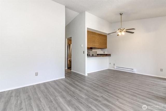 unfurnished living room with baseboard heating, a ceiling fan, baseboards, wood finished floors, and vaulted ceiling