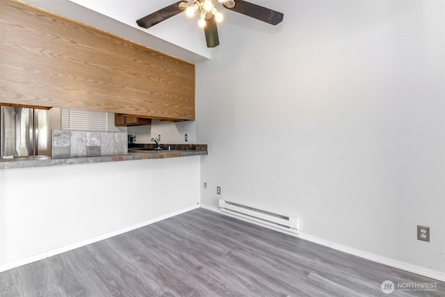 kitchen with baseboards, a ceiling fan, wood finished floors, and baseboard heating