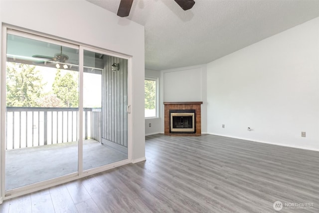 unfurnished living room featuring a ceiling fan, a textured ceiling, wood finished floors, and a tile fireplace