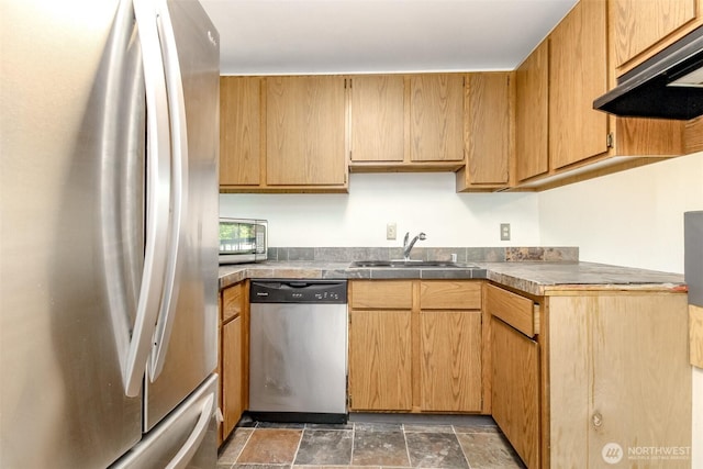 kitchen with a sink, appliances with stainless steel finishes, under cabinet range hood, and stone finish floor