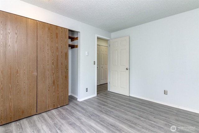 unfurnished bedroom with a closet, baseboards, a textured ceiling, and wood finished floors