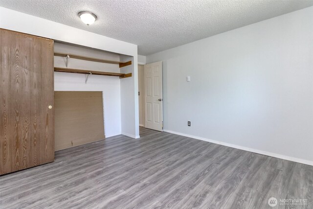 unfurnished bedroom featuring baseboards, a textured ceiling, wood finished floors, and a closet