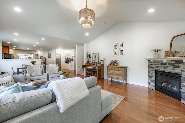 living area with vaulted ceiling, a stone fireplace, recessed lighting, and light wood-style flooring
