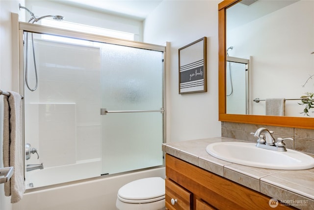 bathroom featuring vanity, decorative backsplash, enclosed tub / shower combo, and toilet