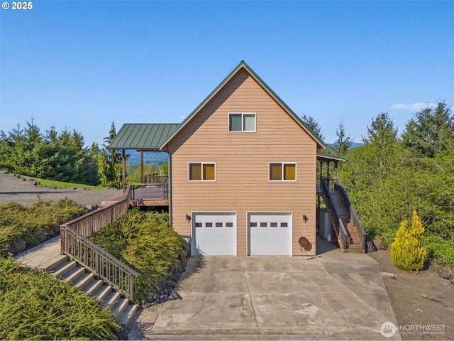 view of side of home with an attached garage, metal roof, driveway, a standing seam roof, and stairs