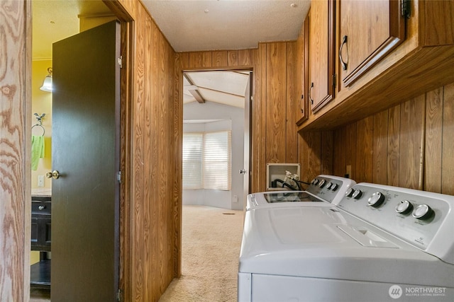 clothes washing area featuring wood walls, cabinet space, washer and dryer, and light carpet