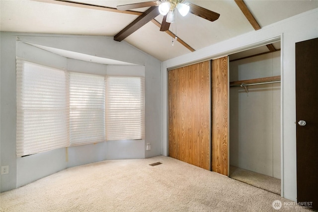 unfurnished bedroom featuring carpet floors, visible vents, a closet, vaulted ceiling with beams, and a ceiling fan
