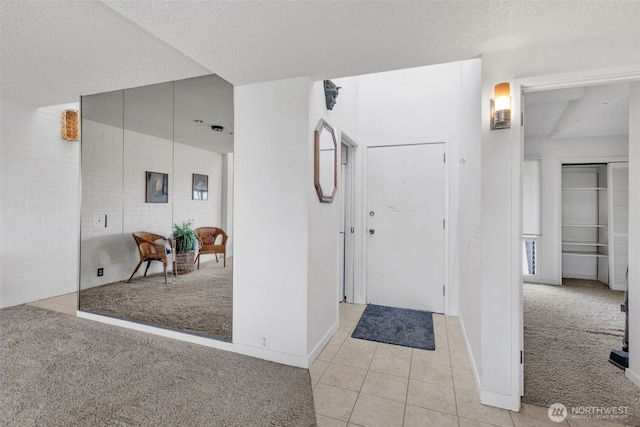 interior space with light colored carpet, baseboards, a textured ceiling, and light tile patterned floors