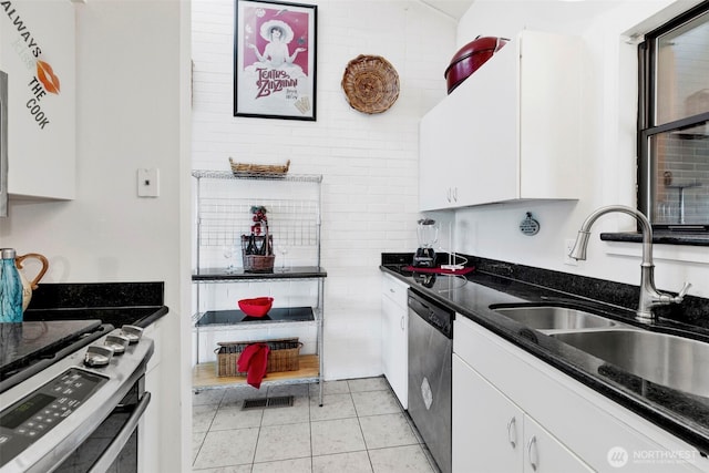 kitchen featuring visible vents, a sink, dark stone counters, stainless steel appliances, and white cabinetry