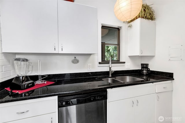 kitchen featuring stainless steel dishwasher, white cabinets, a sink, and dark stone counters