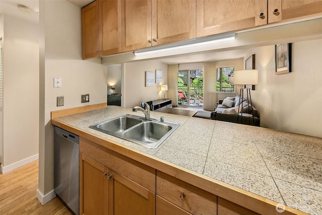 kitchen with dishwasher, a sink, open floor plan, tile counters, and light wood-style flooring