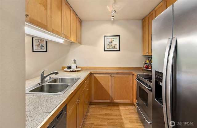 kitchen featuring rail lighting, appliances with stainless steel finishes, a sink, and light wood finished floors