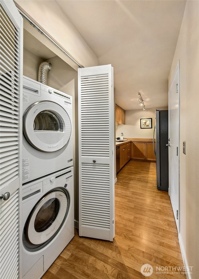 laundry room with laundry area, stacked washer and clothes dryer, light wood finished floors, and rail lighting