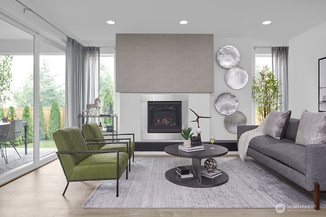 living area featuring recessed lighting, baseboards, a glass covered fireplace, and wood finished floors