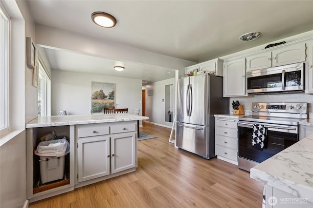 kitchen with stainless steel appliances, light wood-style flooring, a peninsula, baseboards, and light stone countertops