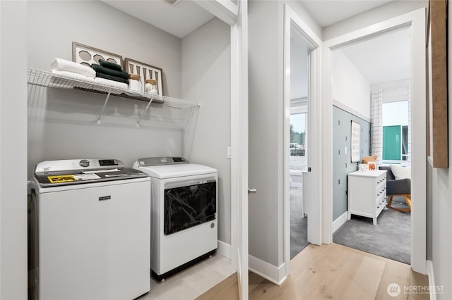 clothes washing area featuring separate washer and dryer, laundry area, baseboards, and light wood finished floors