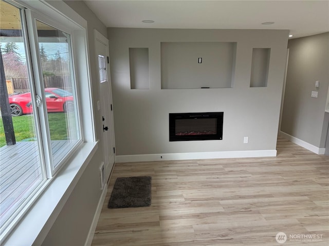 unfurnished living room with a glass covered fireplace, light wood-style flooring, recessed lighting, baseboards, and visible vents