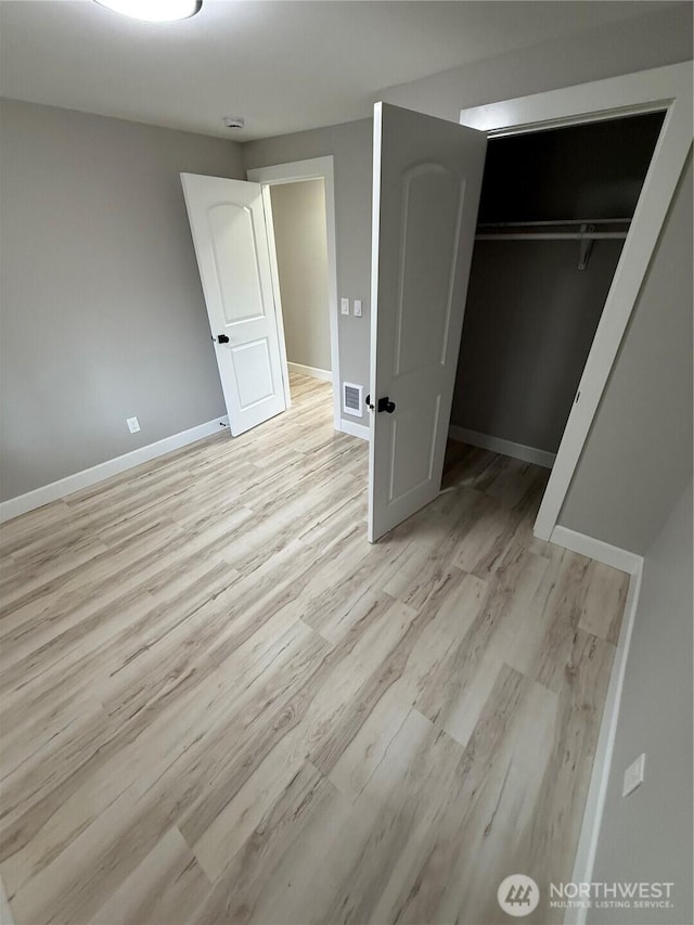 unfurnished bedroom with visible vents, light wood-style flooring, baseboards, and a closet