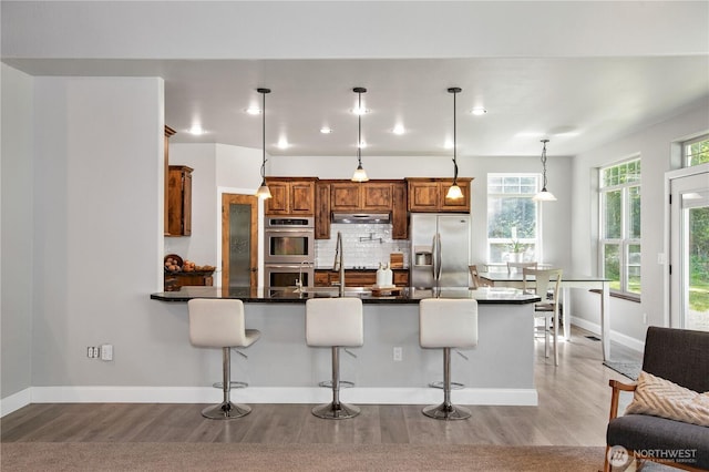 kitchen featuring a breakfast bar, stainless steel appliances, light wood-type flooring, and under cabinet range hood