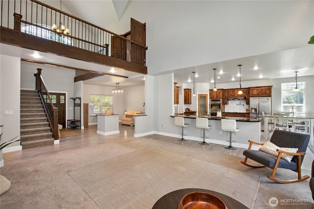living area featuring baseboards, a high ceiling, stairway, light colored carpet, and a notable chandelier