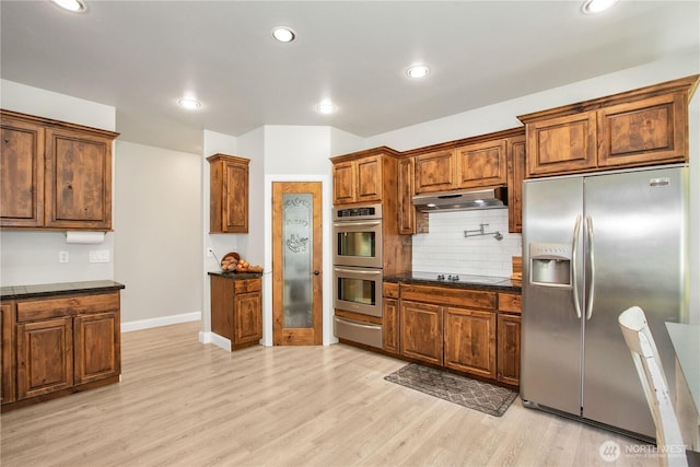 kitchen featuring light wood-style floors, under cabinet range hood, tasteful backsplash, a warming drawer, and stainless steel appliances