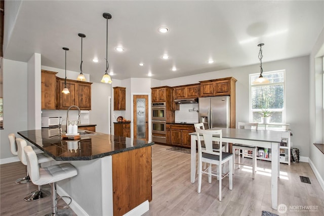 kitchen featuring under cabinet range hood, brown cabinets, a sink, a warming drawer, and stainless steel appliances