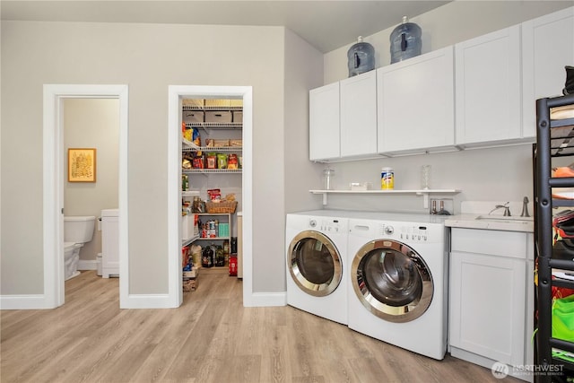 washroom with washing machine and clothes dryer, cabinet space, a sink, baseboards, and light wood-style flooring
