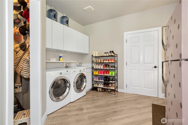 clothes washing area with separate washer and dryer, a sink, cabinet space, and light wood-type flooring