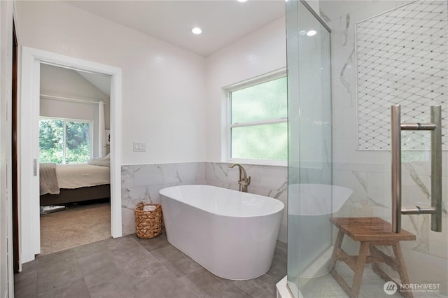 ensuite bathroom featuring ensuite bathroom, tile walls, plenty of natural light, and a soaking tub