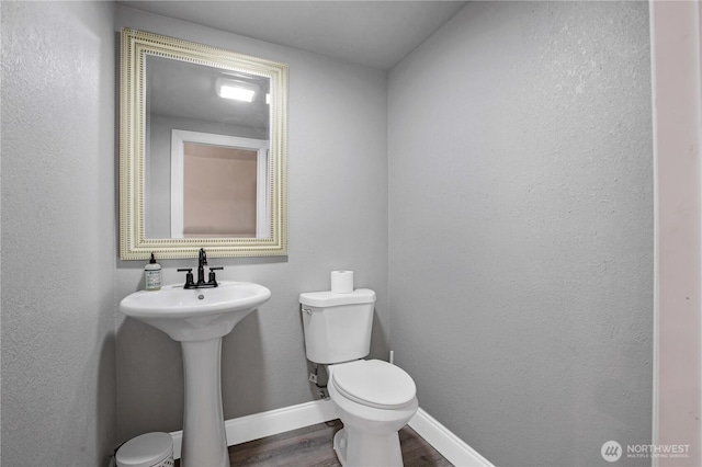 half bath with toilet, baseboards, and wood finished floors
