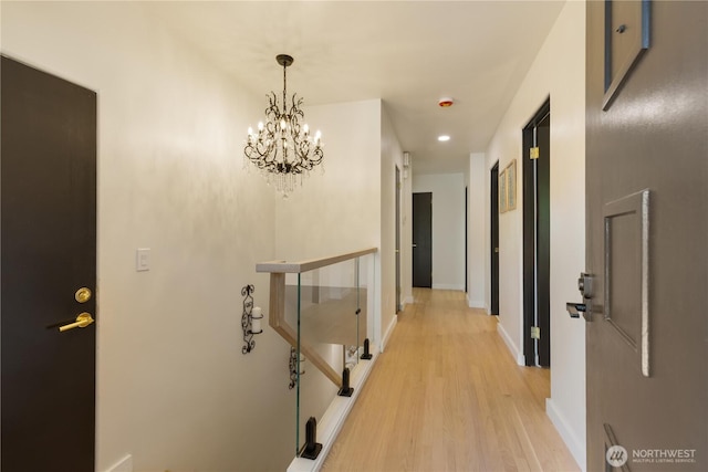 hall featuring an upstairs landing, baseboards, a notable chandelier, recessed lighting, and light wood-style flooring