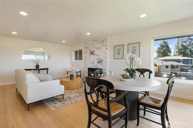 dining space with recessed lighting, light wood-style flooring, a wealth of natural light, and a tile fireplace