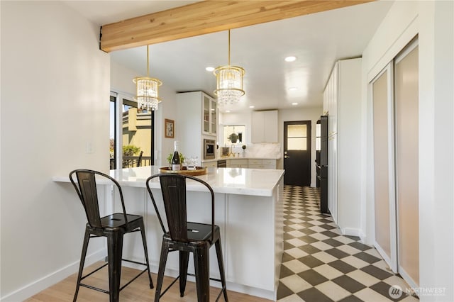 kitchen featuring white cabinets, a kitchen breakfast bar, a chandelier, a peninsula, and glass insert cabinets