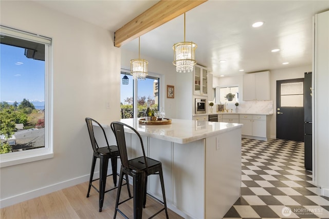 kitchen with a kitchen breakfast bar, a chandelier, white cabinetry, light floors, and glass insert cabinets