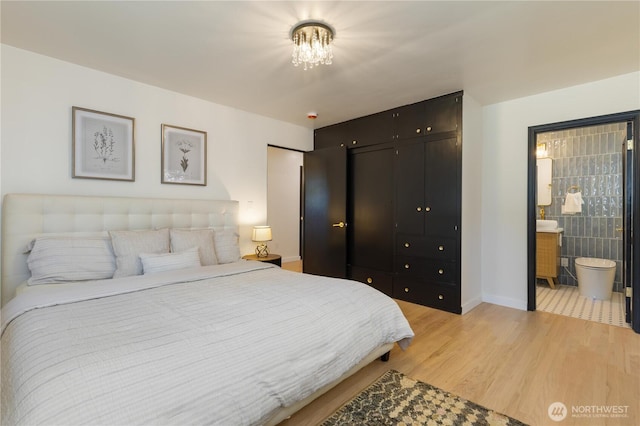 bedroom with baseboards, a chandelier, light wood finished floors, and ensuite bath