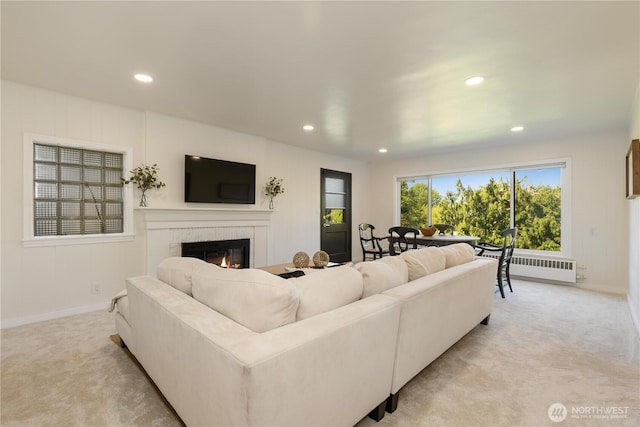 living room featuring a fireplace, baseboards, radiator, light carpet, and recessed lighting