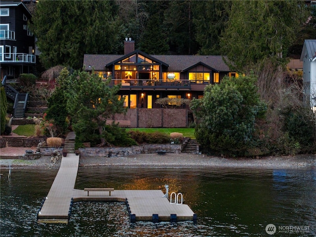 back of property with a water view, a chimney, stairway, and a balcony