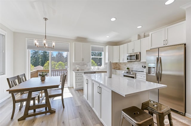 kitchen featuring light wood finished floors, an inviting chandelier, decorative backsplash, a center island, and appliances with stainless steel finishes