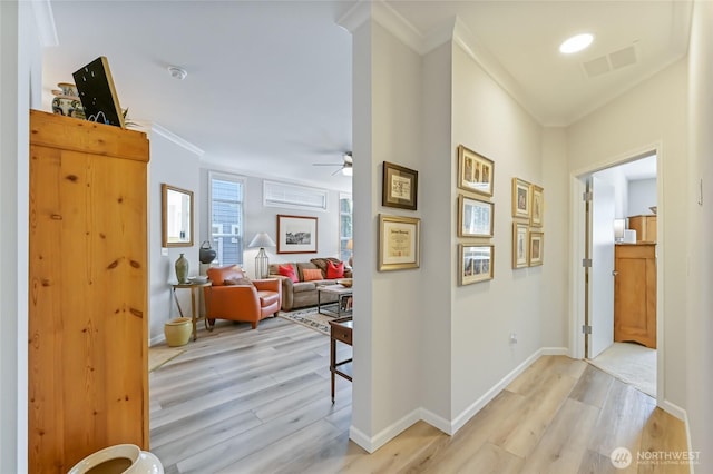 corridor with light wood finished floors, crown molding, visible vents, and baseboards
